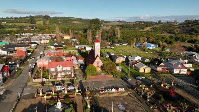 Colorful traditional houses surround a stone church with its tall bell tower in the small town of Curaco de V&eacute;lez, rolling green countryside stretching toward the horizon in Chilo&eacute;.