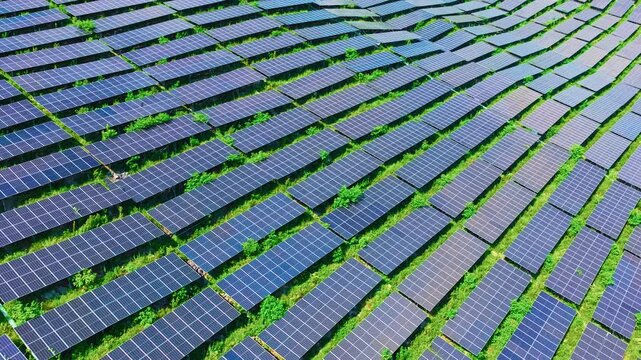 High angle aerial view shows solar power station modules installed in neat repeating rows across a hillside under daylight.