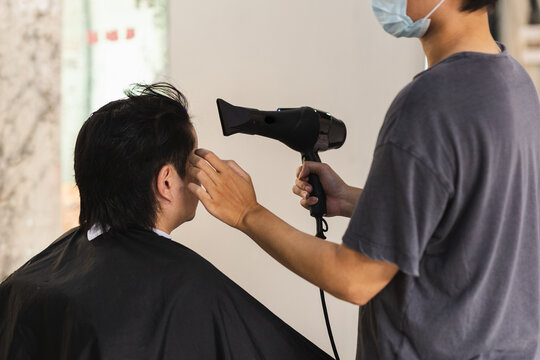 Hairstylist blow drying and shaping a client's hair in a salon.