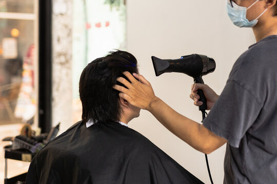 Professional hairstylist using electric hair clippers to trim and shape a client in hair salon.