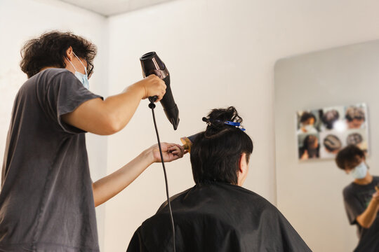 Professional male hairstylist blow drying client's hair in hair salon.