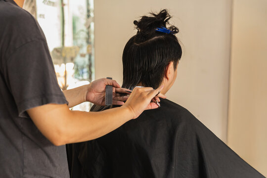 Professional hairstylist cutting hair with scissors in hair salon.