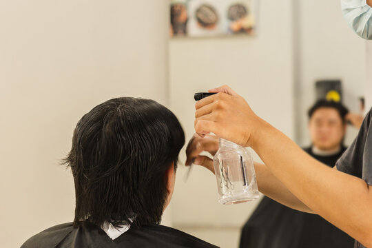 Hairstylist spraying water onto a client's hair using a spray bottle  in salon setting.