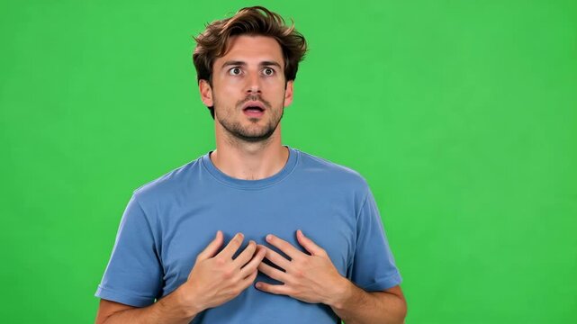 Shocked young man reacting with wide eyes and hands on chest against green screen, surprised emotional reaction for chroma key video