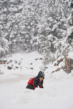 Boy playing in deep snow during heavy snowfall in winter forest