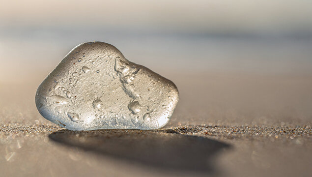 A weathered piece of frosted sea glass rests on a sandy beach casting a shadow