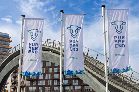 Purmerend, Netherlands - 27 September 2026: Three white city flags with the Purmerend logo waving in the wind in front of the modern Melkwegbrug bridge arch and buildings.