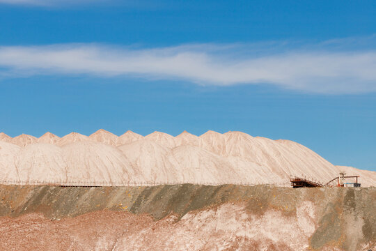 Multi layered white and brown salt slag heaps of a potash mining quarry with a rhythmic peaked ridge under a bright blue sky with thin clouds horizontal view