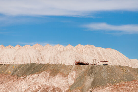Multi layered white and brown salt slag heaps of a potash mining quarry with a rhythmic peaked ridge and technical machinery on top under a blue sky horizontal view