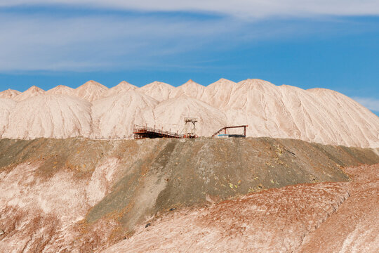 Multi layered white and brown salt slag heaps of a potash mining quarry with a rhythmic peaked ridge and conveyor equipment under a bright blue sky horizontal telephoto view