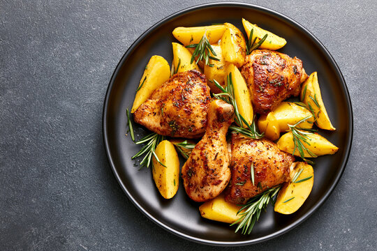 A high angle shot of roasted chicken and potatoes served on a round black plate.