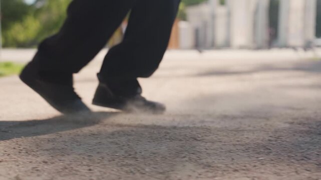 Focus remains fixed low to ground capturing continuous foot movements across rough outdoor path. Legs clad in dark pants stride forward shoes make contact with gravelly surface creating
