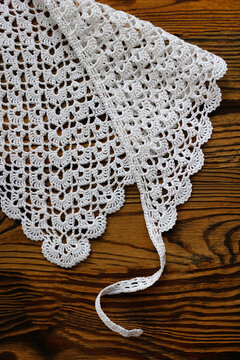 Elegant white handmade crochet lace with delicate scalloped border pattern laid on a rustic dark wooden table. Perfect background texture for craft, vintage, needlework, and home decor projects.
