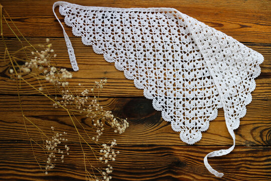 Delicate white handmade crochet lace kerchief scarf paired with gentle dried gypsophila flowers on a dark rustic wooden background. Romantic boho vintage fashion and lifestyle flat lay.
