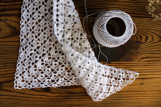 Close up of a white handmade crocheted lace piece with a wooden crochet hook on a dark rustic wooden background. Creative handcraft, needlework, DIY, and vintage hobby concept photography.