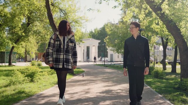 Woman and man walk together on path through greenery. They maintain space between them as they move along tree lined route plaid jacket black park outdoor