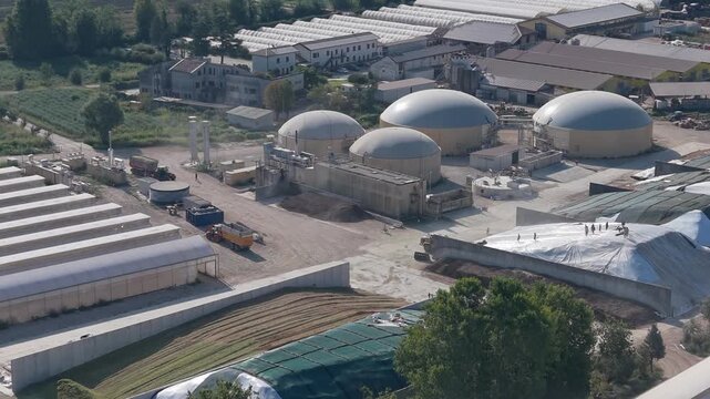 Morning aerial view of a modern livestock farm with anaerobic digesters, silage pits, tractors, greenhouses and solar panels. 
