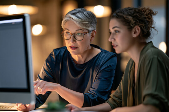 Experienced professional woman collaborating with younger colleague on AI assisted work highlighting responsible technology and intergenerational knowledge sharing