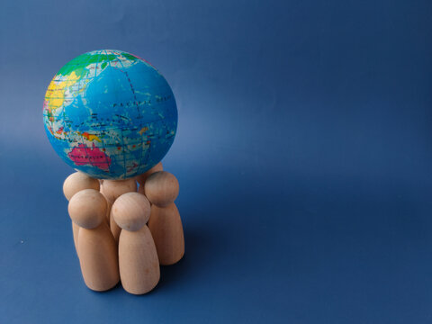 A cluster of wooden peg figures stands together while supporting a small globe on a blue background