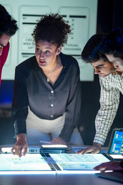 A design team works over the illuminated layout table and the flow finally makes sense inside a dark modern design studio during a focused late-night working session