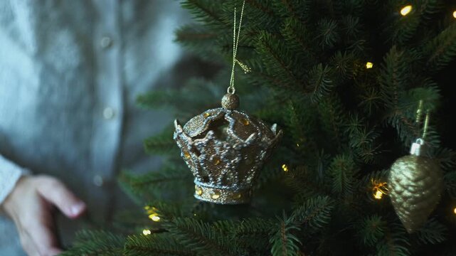 Hands hanging Christmas ornaments on Christmas tree. 