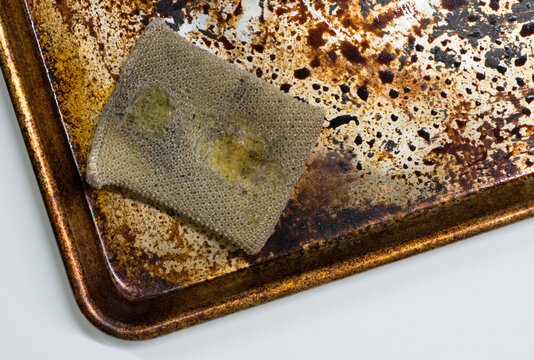 Dirty stained cookie sheet aluminum baking pan bakeware with old cleaning sponge.