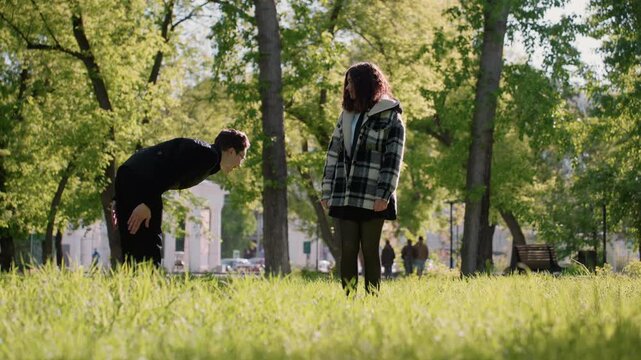 Two people interact in park setting with greenery and sunlight. They engage through gestures while exchanging objects woman man interaction gaze exchange