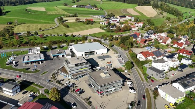 Expanding Commercial Zone and Road Infrastructure in Ravensburg District. Overhead drone panoramic flight panning across a developing commercial area, industrial buildings, gas station, and traffic ne