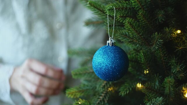 Person decorating Christmas tree with blue Christmas ornaments. 