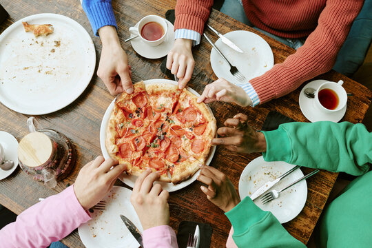 Diverse young adult friends sharing pizza around cafe table. Concept ideal for restaurant marketing, social media promotion and food delivery campaigns, top view