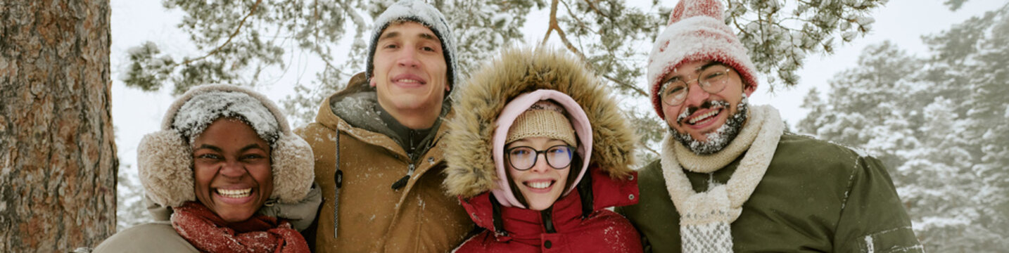Header portrait of diverse multiethnic young adults smiling outdoors in snowy winter forest. Suitable for winter tourism promotion, holiday campaign and seasonal marketing