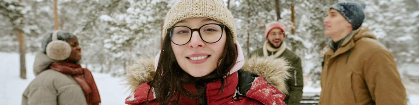 Header portrait of smiling young adult Caucasian woman with multiethnic friends walking in snowy winter forest. Visual representing winter travel and friendship campaigns