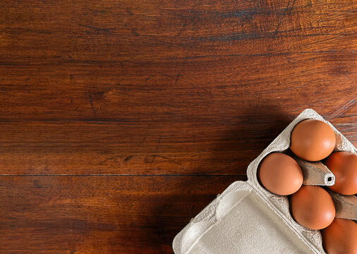 Brown chicken eggs in a cardboard carton on a rustic wooden table background with copy space. Top view.