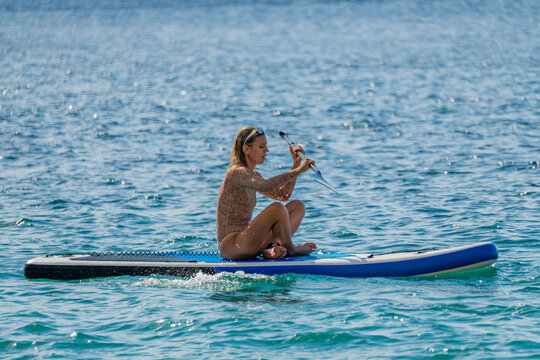 Woman, paddleboard, ocean. Young woman paddling a stand-up paddleboard on the clear blue ocean enjoying summer vacation water sports activity