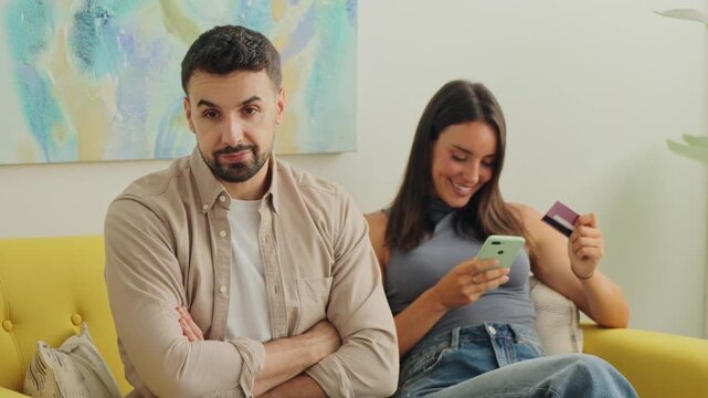 Bright room daylight highlights a couple on a yellow sofa using phones and handling cards in a gentle cheerful mood with a casual real life vibe