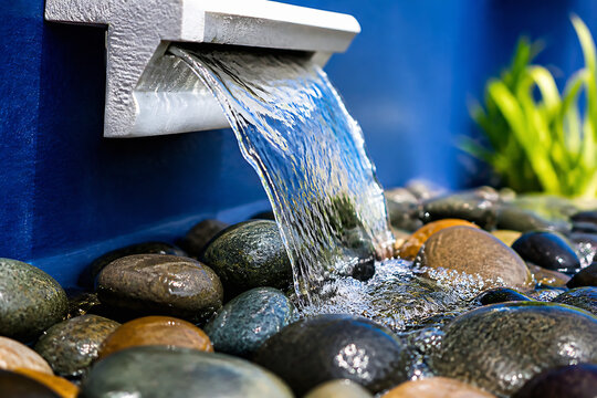 A stream of water flows from a faucet into a collection of smooth, wet stones outdoors.