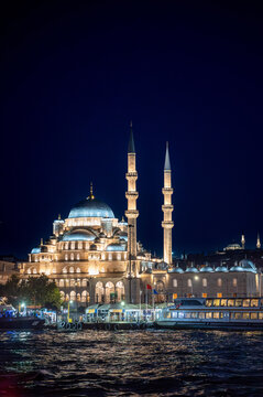 Istanbul,turkey,august 4, 2025. Yeni cami mosque showing its historic architecture and minarets, glowing brightly at night by the bosphorus in eminonu
