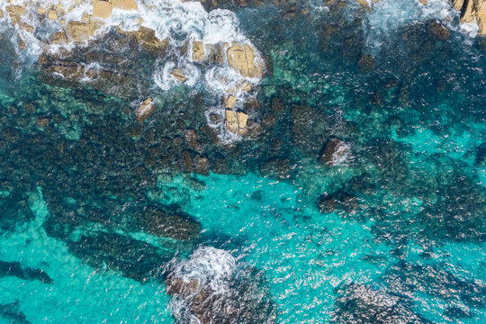Aerial downward view of clear turquoise water meeting the rocky shoreline at Trial Bay near South West Rocks, New South Wales, Australia. 