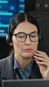 Vertical shot of young adult Caucasian woman wearing headset providing technical support in cybersecurity office. Ideal for corporate video campaigns or tech customer service promotions