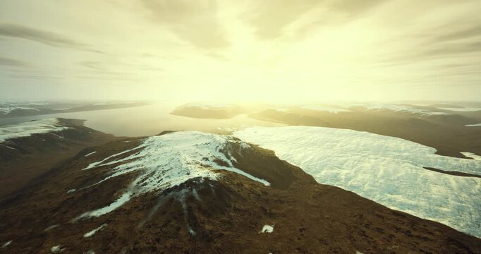 sunlit snow capped ridge and glacier, broad aerial vista with golden light, low clouds, distant horizon, untouched tundra, crisp atmosphere and serene isolation