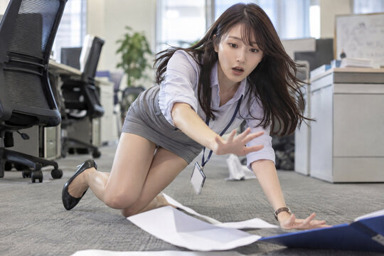 灰色スカートの女性がオフィスの床で青いファイルに手を伸ばす