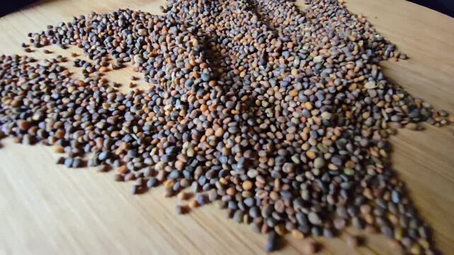 Creative arrangement of organic arugula seeds spread across a textured wooden background, showcasing natural patterns and rich details for gardening and agriculture concepts.   