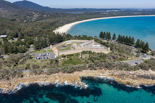 Aerial view of Laggers Point featuring historic Trial Bay Gaol, turquoise coastal waters, sandy shoreline and forested mountains near South West Rocks, New South Wales, Australia.