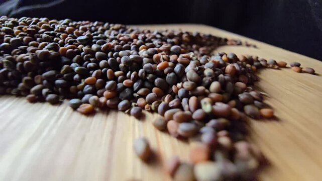 Close-up shot of raw organic arugula seeds neatly piled on a wooden background, showcasing their natural texture and earthy brown color, perfect for healthy food and gardening concepts.   