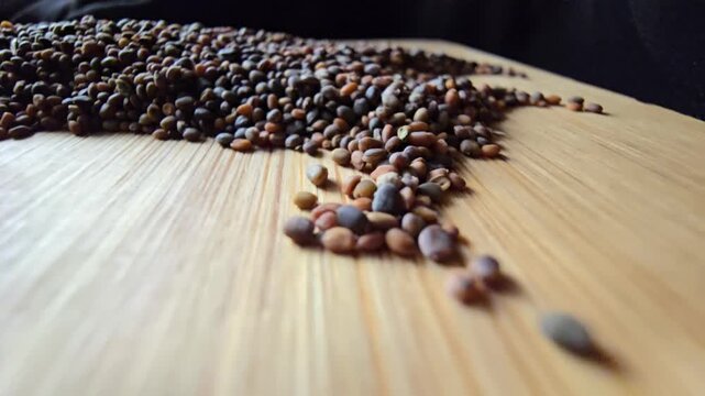 Close-up macro video of raw arugula seeds piled on a wooden surface, showing detailed textures for organic agriculture and nutrition.