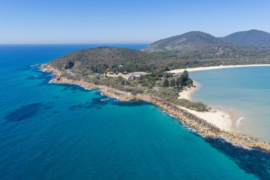 Aerial view over Laggers Point and Front Beach, surrounded by clear turquoise waters and backed by forested mountains at South West Rocks, New South Wales, Australia.