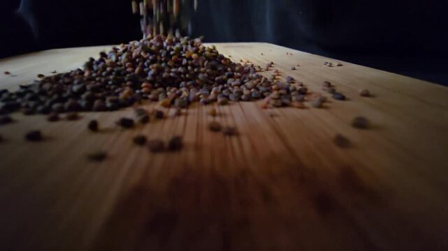 Macro shot of organic arugula and rocket seeds pouring and falling onto a wooden surface, creating a dynamic motion for agricultural and food themes.   