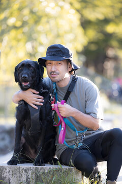 [晩夏～秋イメージ]大型犬と顔を寄せてカメラ目線で笑顔の日本人男性、犬と飼い主の絆、信頼やコミュニケーションイメージ　縦