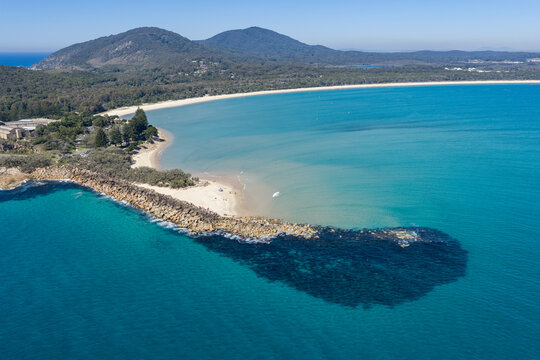 Aerial view over Laggers Point and Front Beach, surrounded by clear turquoise waters and backed by forested mountains at South West Rocks, New South Wales, Australia.