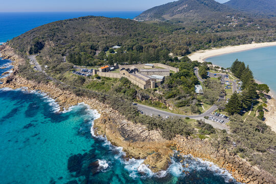 Aerial view of Laggers Point featuring the historic Trial Bay Gaol, rugged coastline, turquoise ocean and forested mountains near South West Rocks, New South Wales, Australia.